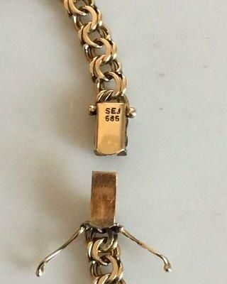 Närbild på låset till ett bismarckhalsband i guld med stämplar.